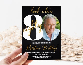 May include: Black and white birthday invitation with a gold inscription that reads "look who's eighty". The invitation features a large white number 80 with a photo of a man in the center. The text "Please join us to celebrate Matthew's Birthday!" is written in gold script. The date, time, and location are listed below.