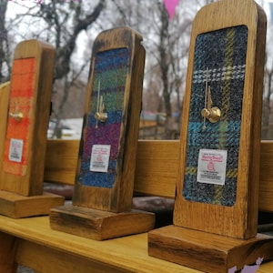 Puede incluir: Relojes enmarcados en madera con caras de tela a cuadros coloridos. Los relojes tienen manecillas de latón y se exhiben en un banco de madera. Los relojes son rectangulares.
