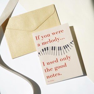 May include: A greeting card with the text "If you were a melody... I used only the good notes." The card features a piano keys design and is accompanied by a tan envelope and a ribbon.
