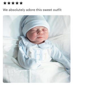 May include: A newborn baby wearing a light blue outfit and matching cap. The outfit features a Peter Pan collar, long sleeves, and an embroidered "H" with two animal figures. The text "We absolutely adore this sweet outfit" is above the baby.
