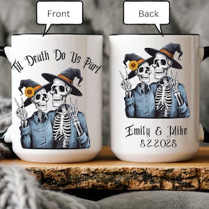 May include: White ceramic coffee mug with a black handle. The front of the mug features a graphic of two skeletons dressed as witches with the text "Til Death Do Us Part". The back of the mug has the text "Emily & Mike 8.2.2023".
