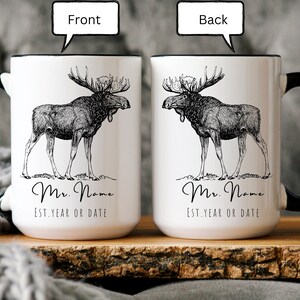 May include: White ceramic mug with a black handle and rim, featuring a detailed black and white illustration of a moose. The mug has the text "Mr. Name" and "Est. Year or Date" in a script font. The image shows the front and back of the mug.