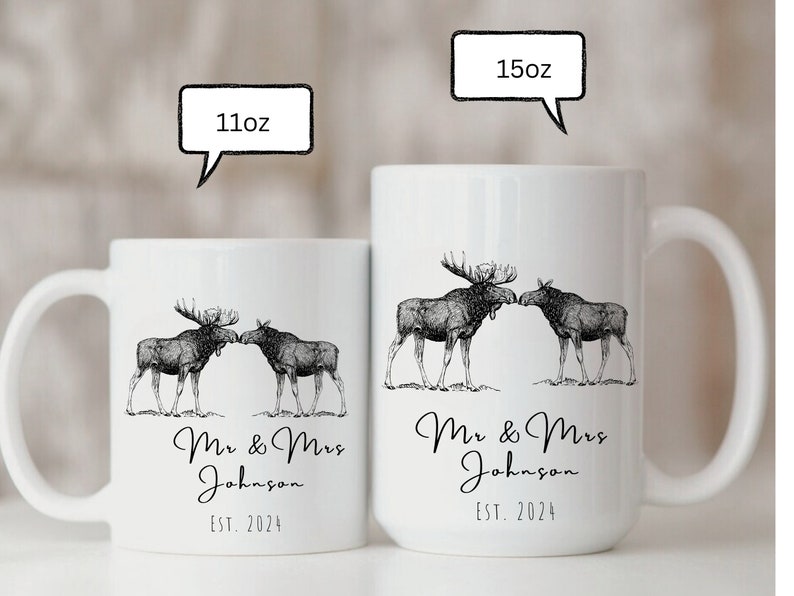 May include: White ceramic mugs with a black and white illustration of two moose touching noses. The mugs are labeled "11oz" and "15oz" and feature the text "Mr & Mrs Johnson EST. 2024".