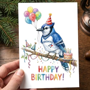 May include: A watercolour birthday card showing a blue jay in a Toronto jersey and party hat, holding balloons. The card says "HAPPY BIRTHDAY!" in colourful letters, with a small cake and confetti.