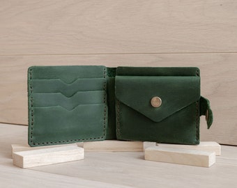 May include: A dark green leather wallet with multiple card slots and a flap pocket with a button closure. The wallet is open and lying on a wooden surface.