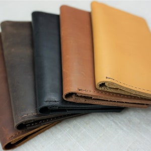 Puede incluir: Cinco carteras de cuero en diferentes colores, incluyendo marr&oacute;n, negro, marr&oacute;n claro y un marr&oacute;n m&aacute;s claro. Las carteras est&aacute;n apiladas una encima de la otra, con la cartera superior siendo del color m&aacute;s claro.