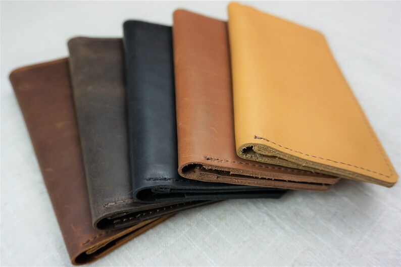 Puede incluir: Cinco carteras de cuero en diferentes colores, incluyendo marr&oacute;n, negro, marr&oacute;n claro y un marr&oacute;n m&aacute;s claro. Las carteras est&aacute;n apiladas una encima de la otra, con la cartera superior siendo del color m&aacute;s claro.