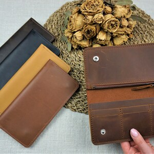 Puede incluir: Cuatro carteras de cuero en diferentes colores: marr&oacute;n, beige, azul marino y negro. La cartera marr&oacute;n est&aacute; abierta para mostrar el interior con m&uacute;ltiples ranuras para tarjetas y un bolsillo con cremallera.