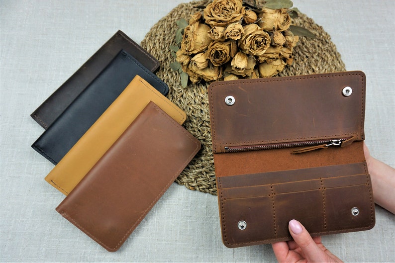Puede incluir: Cuatro carteras de cuero en diferentes colores: marr&oacute;n, beige, azul marino y negro. La cartera marr&oacute;n est&aacute; abierta para mostrar el interior con m&uacute;ltiples ranuras para tarjetas y un bolsillo con cremallera.