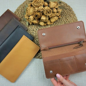 Puede incluir: Cuatro carteras de cuero en diferentes colores: marr&oacute;n, negro, marr&oacute;n oscuro y beige. La cartera beige est&aacute; abierta, mostrando un compartimento con cremallera y tres ranuras para tarjetas.