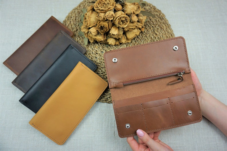 Puede incluir: Cuatro carteras de cuero en diferentes colores: marr&oacute;n, negro, marr&oacute;n oscuro y beige. La cartera beige est&aacute; abierta, mostrando un compartimento con cremallera y tres ranuras para tarjetas.