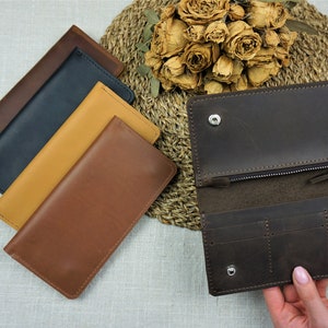 Puede incluir: Cuatro carteras de cuero en diferentes colores, incluyendo marr&oacute;n, beige, negro y azul marino. Una cartera marr&oacute;n est&aacute; abierta para mostrar su interior con m&uacute;ltiples ranuras para tarjetas y un compartimento con cremallera.