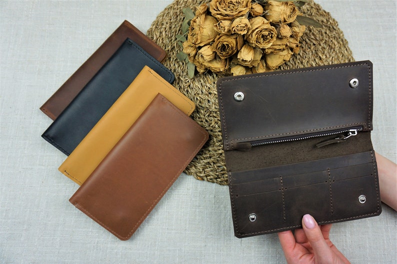 Puede incluir: Cuatro carteras de cuero en diferentes colores, incluyendo marr&oacute;n, beige, negro y azul marino. Una cartera marr&oacute;n est&aacute; abierta para mostrar su interior con m&uacute;ltiples ranuras para tarjetas y un compartimento con cremallera.