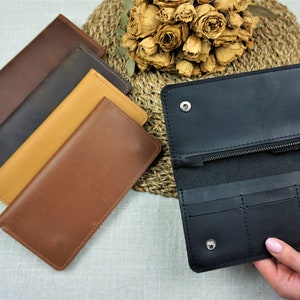 Puede incluir: Cuatro carteras de cuero en diferentes colores: marr&oacute;n, marr&oacute;n oscuro, beige y negro. La cartera negra est&aacute; abierta, mostrando su interior con m&uacute;ltiples ranuras para tarjetas y un compartimento con cremallera.