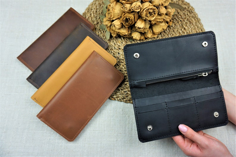 Puede incluir: Cuatro carteras de cuero en diferentes colores: marr&oacute;n, marr&oacute;n oscuro, beige y negro. La cartera negra est&aacute; abierta, mostrando su interior con m&uacute;ltiples ranuras para tarjetas y un compartimento con cremallera.