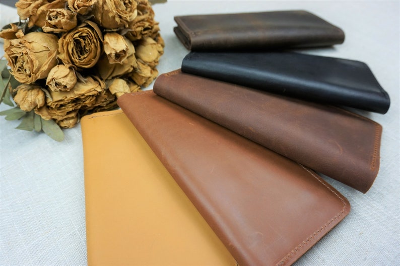 Puede incluir: Cinco carteras de cuero en diferentes colores, incluyendo marr&oacute;n, negro, beige y un marr&oacute;n m&aacute;s claro. Las carteras est&aacute;n apiladas una encima de la otra, con la cartera marr&oacute;n en la parte superior.