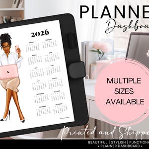 May include: A black planner with a 2026 calendar page. The calendar page features an illustration of a person holding a phone and a pink laptop. The text "PLANNER Dashboard" and "MULTIPLE SIZES AVAILABLE" are also visible.
