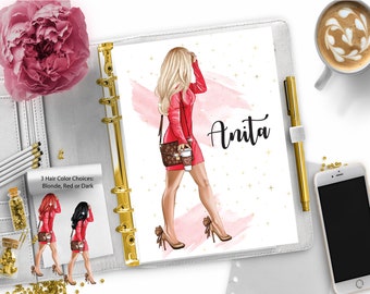 May include: A white planner with a gold ring binder. The planner has a pink watercolor background with gold stars. A woman with blonde hair is illustrated wearing a red dress and holding a coffee cup. The text "Anita" is written in black cursive on the planner.