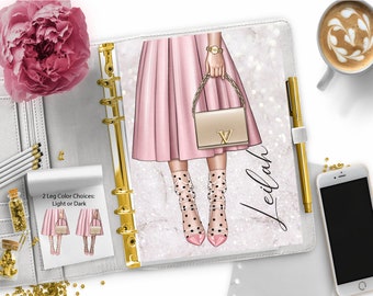 May include: A white planner with a gold ring binder and a pink and white illustration of a woman wearing a pink skirt, black and white polka dot stockings, and pink heels. The woman is holding a beige handbag with a gold chain strap. The planner has the word "Leilah" written on it in gold script. The planner has a note attached to it that says "2 Leg Color Choices: Light or Dark".