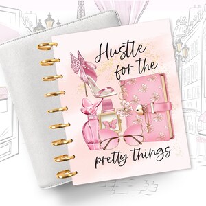 May include: A pink and gold planner with the text "Hustle for the pretty things" and illustrations of a high heel shoe, perfume bottle, sunglasses, and a pink notebook with a lock and key.