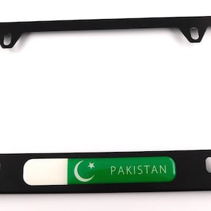 May include: Black license plate frame with the flag of Pakistan. The frame has a rectangular shape with rounded corners and mounting holes. The Pakistan flag is green and white with a crescent moon and star.