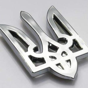May include: A shiny, silver trident emblem with a three-pronged design and a decorative base. The emblem has a polished, reflective surface, and is set against a light background. The emblem is a symbol of Ukraine.