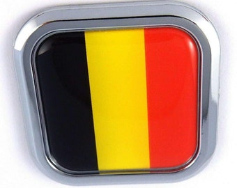 May include: A rectangular emblem with a shiny chrome border. The emblem features the flag of Belgium, with vertical stripes of black, yellow, and red. The design is clean and modern, with a glossy finish.