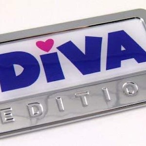 May include: A rectangular, chrome-finished emblem with the word "DIVA" in blue letters and a pink heart above the "I". The word "EDITION" is embossed below. The emblem has a white background.