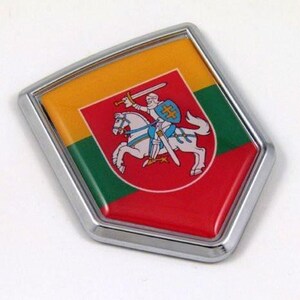 Könnte beinhalten: Ein chromgerahmtes Emblem mit dem litauischen Wappen. Das Emblem hat einen roten, grünen und gelben Hintergrund. Das Wappen zeigt einen Ritter auf einem Pferd mit einem Schwert. Das Emblem ist ein dekorativer Gegenstand.