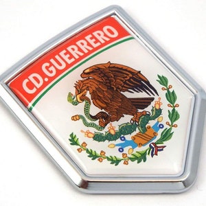 May include: A chrome-framed emblem featuring the Mexican coat of arms. The emblem has a white background with a brown eagle, green cactus, and a snake. The top section is red with the text "CD. GUERRERO".