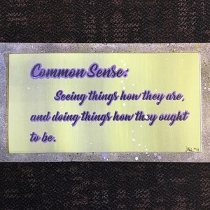 May include: A rectangular artwork with a light green background and a silver frame. The text "Common Sense: Seeing things how they are, and doing things how they ought to be" is written in purple script. The artwork is signed "JAL '17".