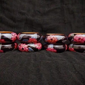 May include: A collection of six dark brown wooden bangles, each adorned with a vibrant floral design. The flowers are primarily pink and red, with accents of blue and white leaves. The bangles are stacked in pairs.