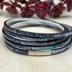 May include: Multi-layered leather bracelet with a silver clasp. The bracelet features a blue and black floral pattern.