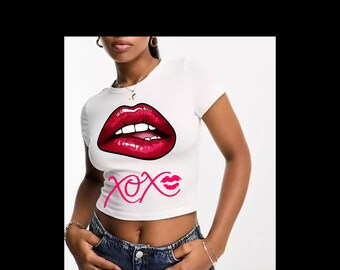 Könnte beinhalten: Weißes Crop-Top mit einer großen Grafik roter Lippen und dem Text "xox" in Pink. Das Top hat kurze Ärmel und einen runden Ausschnitt. Das Model trägt eine blaue Jeans.