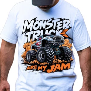 以下が含まれることがあります： 白いTシャツ。モンスター・トラックのグラフィックと「MONSTER TRUCK ARE MY JAM」の文字。モンスター・トラックはグレーと赤で、オレンジ色の砂埃が舞っている。半袖のTシャツ。