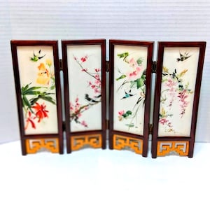 May include: A miniature folding screen with four panels. Each panel features a different floral and bird design in shades of red, yellow, pink, and green. The frames are dark brown, and the base is a light orange color.