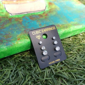 May include: A black card with the text "Cubic Earrings" and "Nickel Free" on it. The card has six pairs of small, clear cubic zirconia earrings.