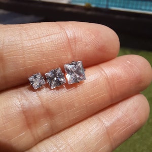 May include: Three silver square-shaped earrings with clear cubic zirconia stones. The earrings are arranged in order of size, with the largest earring on the left and the smallest earring on the right.