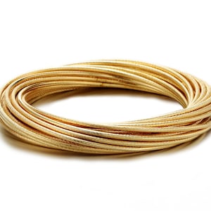 May include: A gold-colored metal bangle bracelet made of multiple thin, braided strands.