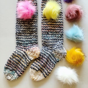 May include: Two pairs of striped knit socks with colorful pom poms attached. The pom poms are in pink, yellow, purple, light blue, white, and yellow.