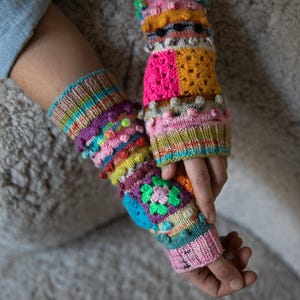 Puede incluir: Un par de calentadores de brazo de punto coloridos. Los calentadores de brazo presentan una variedad de colores que incluyen rosa, verde, amarillo, morado y azul. Tienen un diseño texturizado con bolitas y motivos florales. Los calentadores de brazo están hechos a mano.
