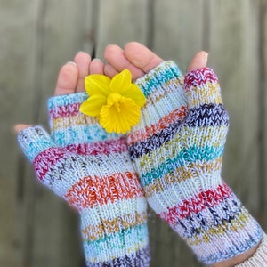 May include: A pair of colorful striped fingerless gloves with a yellow daffodil flower in the center.