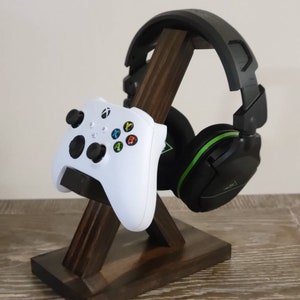 May include: A wooden stand with a white video game controller and black headphones. The stand is made of dark brown wood and has a triangular shape.