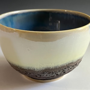 May include: A ceramic bowl with a light yellow glaze and a dark brown speckled rim. The inside of the bowl is glazed in a deep blue color.