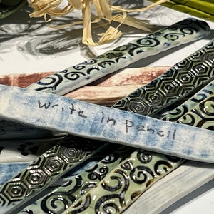 May include: A set of ceramic tiles with different patterns, including swirls, hexagons, and a blue tile with the words "Write in pencil" written on it.