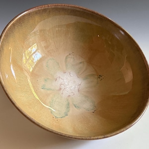 May include: A handmade ceramic bowl with a floral design. The bowl has a light brown exterior and a cream-colored interior with a green and white floral pattern. The bowl is oval-shaped and appears to be glazed.