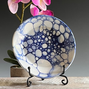 May include: A white ceramic plate with a blue and white bubble design. The plate is on a black metal stand.