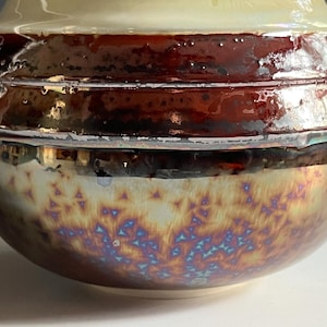 May include: A ceramic bowl with a brown and iridescent glaze. The bowl has a rounded shape and a wide rim.