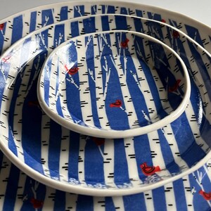 May include: Set of three blue and white ceramic plates with a birch tree and cardinal design.
