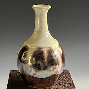 May include: A small, round ceramic vase with a narrow neck. The vase has a white glaze with brown and gold iridescent accents.